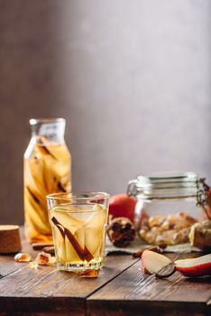 Flavored Water in Glass and Bottle with Sliced Pear, Cinnamon Stick, Ginger Root and Some Sugar. Ingredients on Wooden Table. Vertical Orientation.