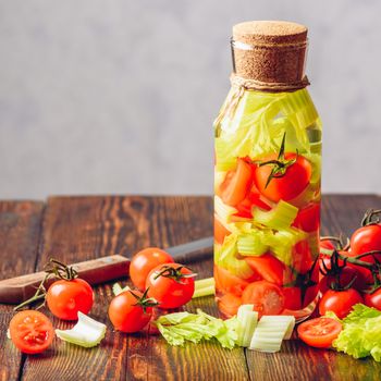 Bottle of Flavored Water with Vegetables: Cherry Tomato and Celery Stems. Ingredients and Knife on Wooden Table. Copy Space.
