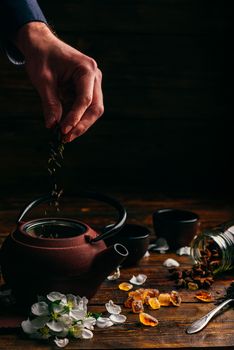 Tea Preparing. Hand Puts Dry Tea to Teapot. Apple Flower, Sugar and Anise Star on Wooden Table.