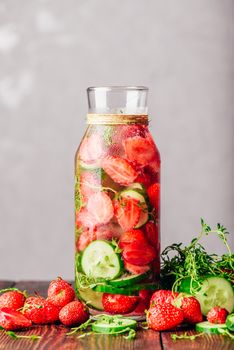 Bottle of Infused Water with Fresh Strawberry, Sliced Cucumber and Springs of Thyme. Ingredients Scattered on Wooden Table. Copy Space and Vertical Orientation.