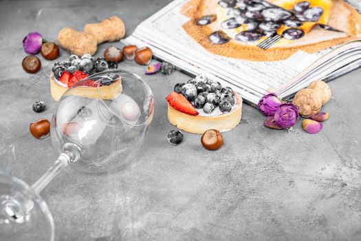 Blueberry and strawberry shortcake. There are hazelnuts, roses and wine corks on the table. Stone gray background.