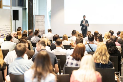 Male speaker giving a talk in conference hall at business event. Audience at the conference hall. Business and Entrepreneurship concept. Focus on unrecognizable people in audience.