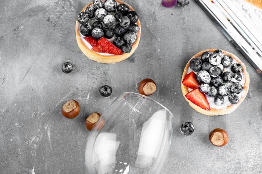 Blueberry and strawberry shortcake. There are hazelnuts, roses and wine corks on the table. Stone gray background.