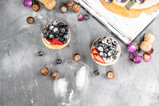 Blueberry and strawberry shortcake. There are hazelnuts, roses and wine corks on the table. Stone gray background.