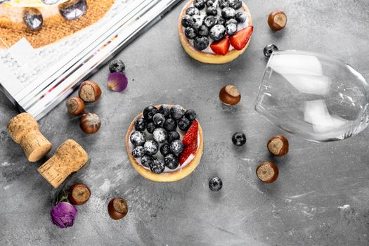 Blueberry and strawberry shortcake. There are hazelnuts, roses and wine corks on the table. Stone gray background.