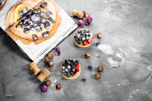 Blueberry and strawberry shortcake. There are hazelnuts, roses and wine corks on the table. Stone gray background.