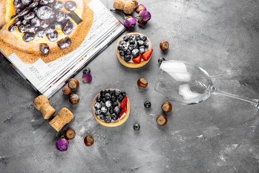 Blueberry and strawberry shortcake. There are hazelnuts, roses and wine corks on the table. Stone gray background.