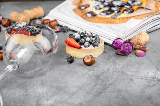 Blueberry and strawberry shortcake. There are hazelnuts, roses and wine corks on the table. Stone gray background.