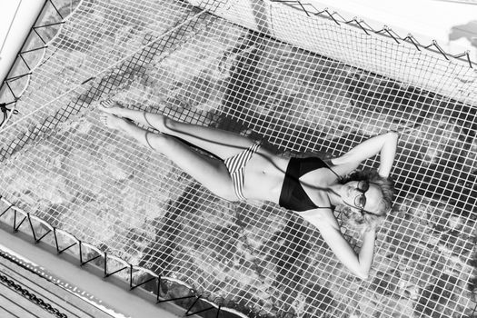 Womanin bikini tanning and relaxing on a summer sailin cruise, lying in hammock of luxury catamaran boat. Black and white image.