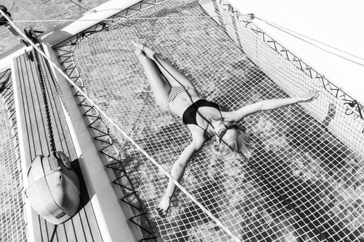 Womanin bikini tanning and relaxing on a summer sailin cruise, lying in hammock of luxury catamaran boat. Black and white image.