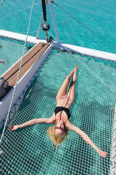 Womanin bikini tanning and relaxing on a summer sailin cruise, lying in hammock of luxury catamaran near picture perfect white sandy beach on Spargi island in Maddalena Archipelago, Sardinia, Italy.