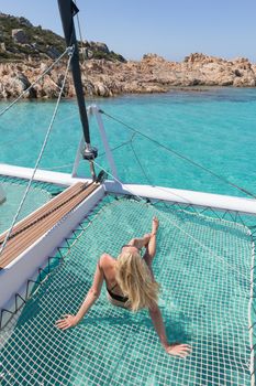 Womanin bikini tanning and relaxing on a summer sailin cruise, lying in hammock of luxury catamaran near picture perfect white sandy beach on Spargi island in Maddalena Archipelago, Sardinia, Italy.