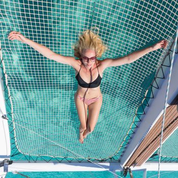 Womanin bikini tanning and relaxing on a summer sailin cruise, lying in hammock of luxury catamaran near picture perfect white sandy beach on Spargi island in Maddalena Archipelago, Sardinia, Italy.