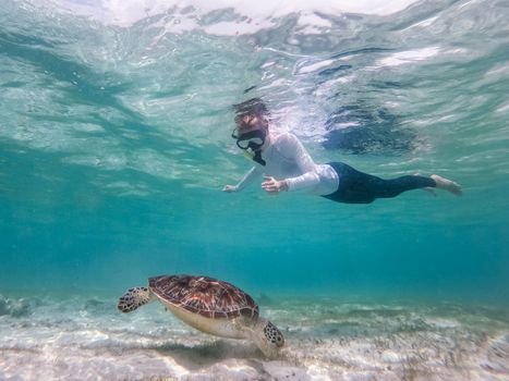 Woman wearing snokeling mask swimming with sea turtle in turquoise blue water of Gili islands, Indonesia. Underwater photo. Hawksbill sea turtle, Eretmochelys imbricata is endangered species.