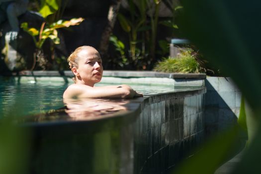 Sensual young woman relaxing in outdoor swimming pool. Wellness and body care concept.