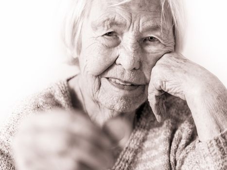 Portrait of sad elderly woman sitting at table at home and looking miserably at only remaining coin from pension in hand. Unsustainability of social transfers and pension system. Selective focus.