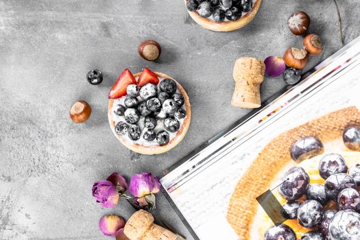 Blueberry and strawberry shortcake. There are hazelnuts, roses and wine corks on the table. Stone gray background.