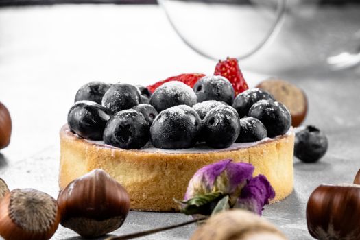 Blueberry and strawberry shortcake. There are hazelnuts, roses and wine corks on the table. Stone gray background.