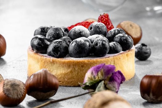 Blueberry and strawberry shortcake. There are hazelnuts, roses and wine corks on the table. Stone gray background.