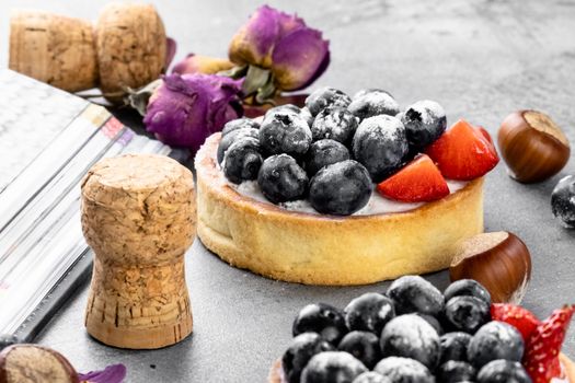 Blueberry and strawberry shortcake. There are hazelnuts, roses and wine corks on the table. Stone gray background.