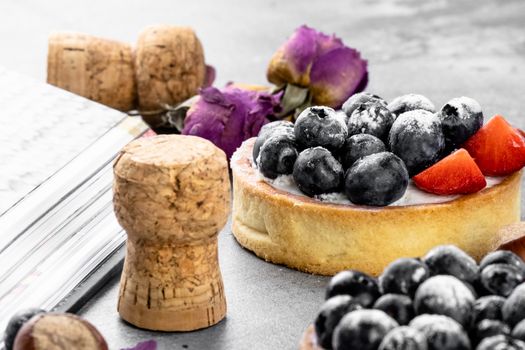 Blueberry and strawberry shortcake. There are hazelnuts, roses and wine corks on the table. Stone gray background.