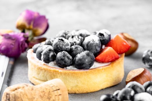 Blueberry and strawberry shortcake. There are hazelnuts, roses and wine corks on the table. Stone gray background.