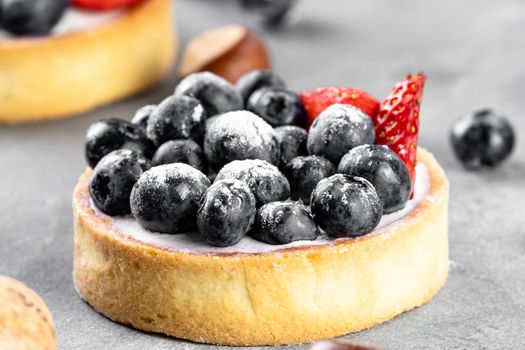 Blueberry and strawberry shortcake. There are hazelnuts, roses and wine corks on the table. Stone gray background.