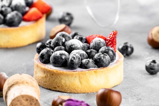 Blueberry and strawberry shortcake. There are hazelnuts, roses and wine corks on the table. Stone gray background.