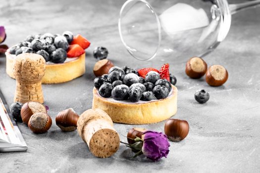 Blueberry and strawberry shortcake. There are hazelnuts, roses and wine corks on the table. Stone gray background.