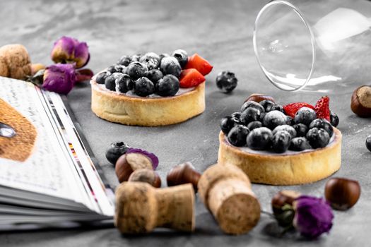 Blueberry and strawberry shortcake. There are hazelnuts, roses and wine corks on the table. Stone gray background.