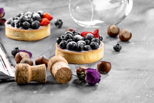 Blueberry and strawberry shortcake. There are hazelnuts, roses and wine corks on the table. Stone gray background.