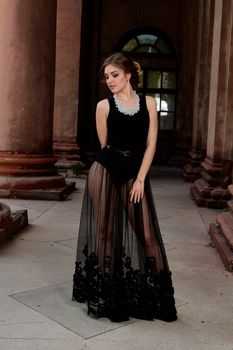 Young woman in sexy transparent black dress near the ancient building. Vintage building. Fashion woman. Young woman modern portrait.