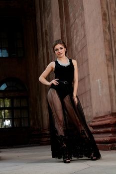 Young woman in sexy transparent black dress near the ancient building. Vintage building. Fashion woman. Young woman modern portrait.