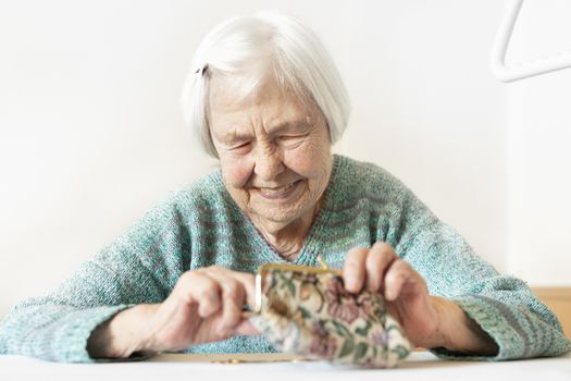 Cheerful elderly 96 years old woman sitting at table at home happy with her pension savings in her wallet after paying bills. Saving for retirement and financial planing concept.