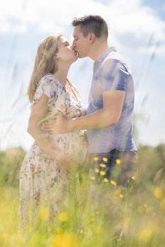 Young happy pregnant couple in love kissing in meadow. Concept of love and family creation.