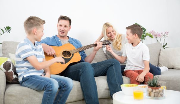 Happy caucasian family smiling while playing guitar and singing songs together at cosy modern home. Spending quality leisure time with children and family concept.