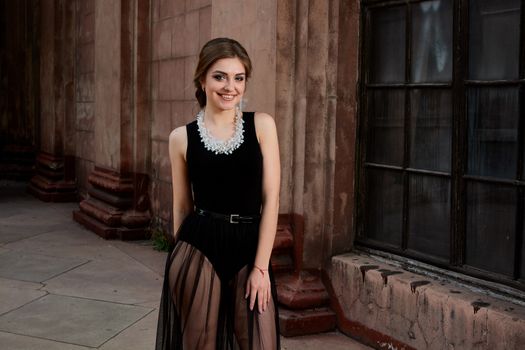 Young woman in sexy transparent black dress near the ancient building. Vintage building. Fashion woman. Young woman modern portrait.