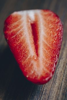 vertical photo of a half strawberry on a wooden table in rustic style