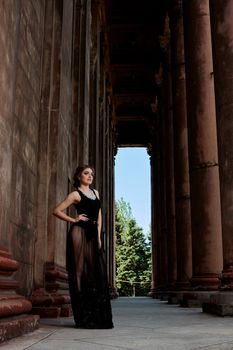 Young woman in sexy transparent black dress near the ancient building. Vintage building. Fashion woman. Young woman modern portrait.