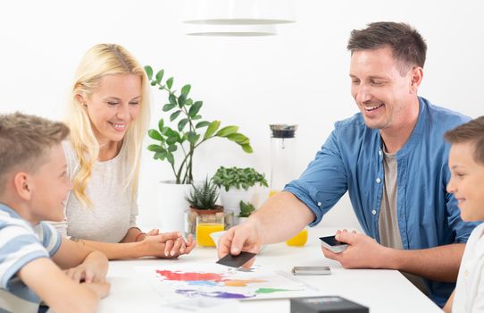 Happy young family playing card game at dining table at bright modern home. Spending quality leisure time with children and family concept. Cards are generic and debranded.