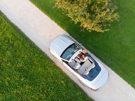 Aerial view of successful man driving and enjoying his silver convertible luxury sports car on the open country side road.