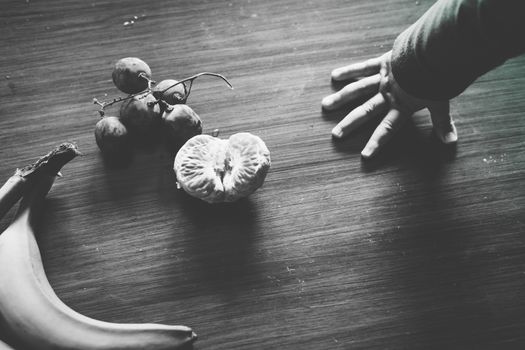 Baby exploring some fruits with his hand on a dark wooden table