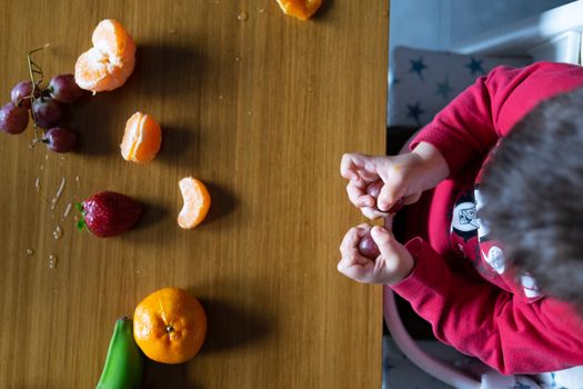 Baby exploring some fruits with his hand on a dark wooden table