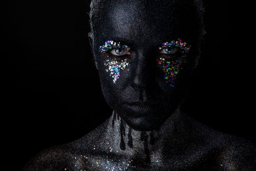 Conceptual art Portrait of Beautiful Woman in Black makeup with Sparkles on a Face isolated on a dark background