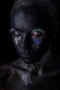 Conceptual art Portrait of Beautiful Woman in Black makeup with Sparkles on a Face isolated on a dark background