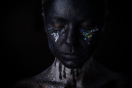 Conceptual art Portrait of Beautiful Woman in Black makeup with Sparkles on a Face isolated on a dark background