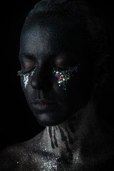 Conceptual art Portrait of Beautiful Woman in Black makeup with Sparkles on a Face isolated on a dark background