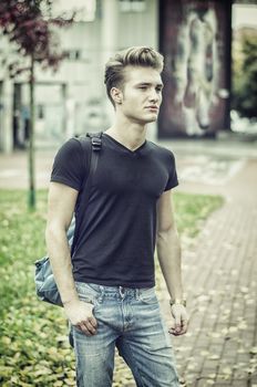 Attractive young man standing in city environment, with rucksack on one shoulder