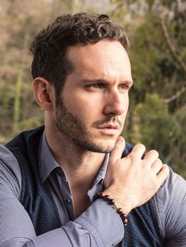 Handsome elegant man outdoor, wearing shirt and vest, looking away to a side