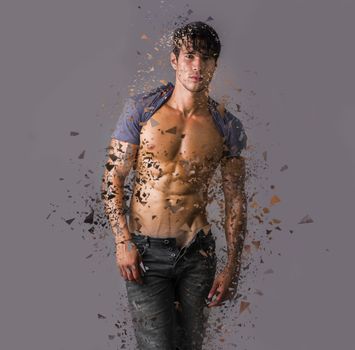 Handsome man with muscular torso standing on gray background in dispersion looking at camera
